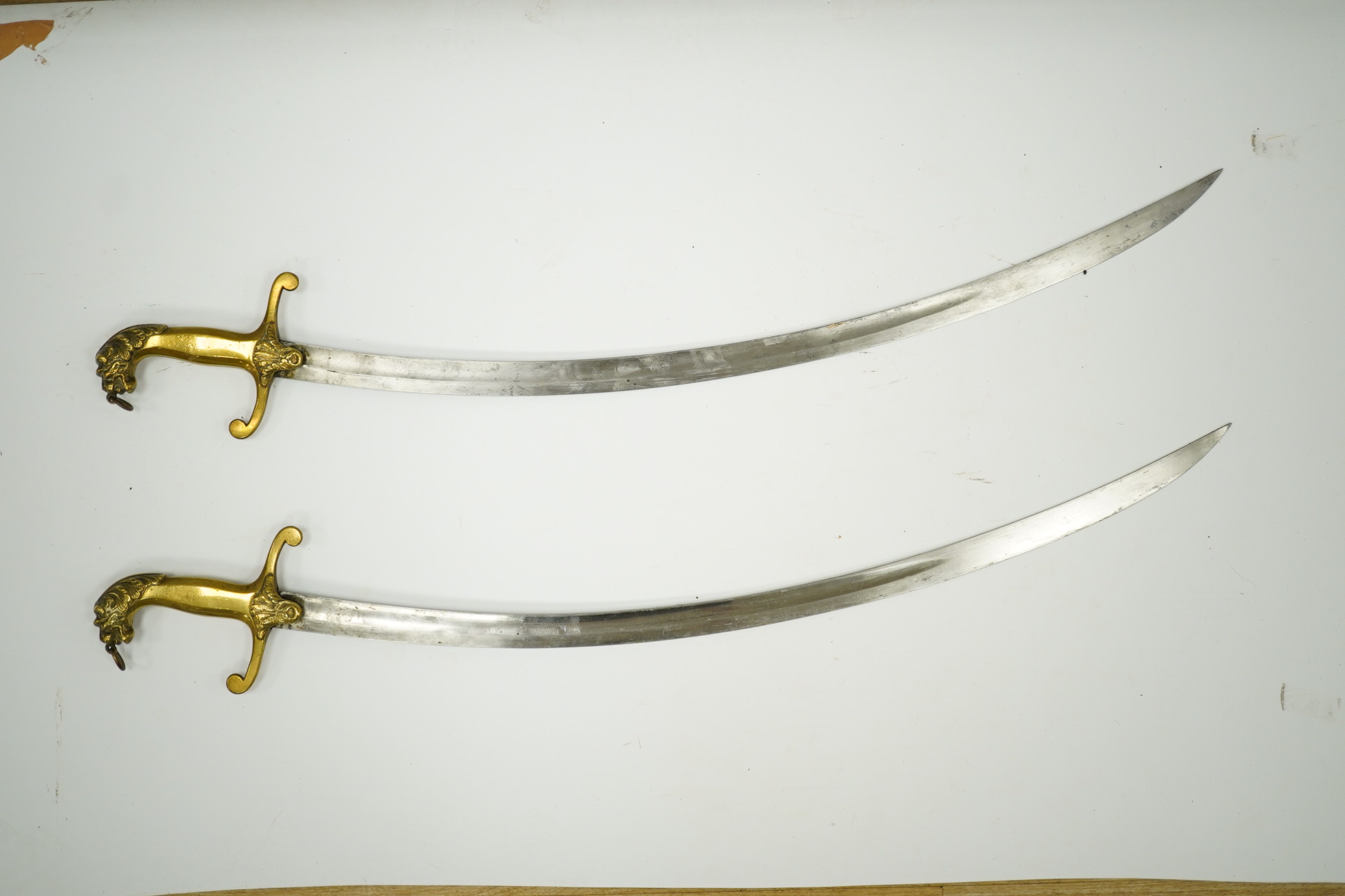 A pair of Victorian bandsman’s swords of Shamshir type, curved single edge blades, cast brass hilts with lions head pommels, in their brass scabbards. Condition - good, some dents to scabbards.